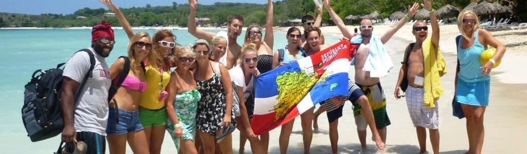 For the new Spanish Course program a group of Spanish students stands on the beach of Punta Rucia during one of IIC Spanish School's social activities, waving the Dominican flag, having fun, and enjoying their time together, experiencing the Dominican Republic's beautiful beaches and the great hospitality of its people while learning Spanish in the Dominican Republic.