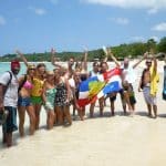 For the new Spanish Course program a group of Spanish students stands on the beach of Punta Rucia during one of IIC Spanish School's social activities, waving the Dominican flag, having fun, and enjoying their time together, experiencing the Dominican Republic's beautiful beaches and the great hospitality of its people while learning Spanish in the Dominican Republic.