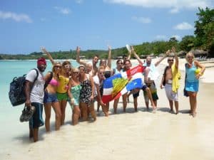 For the new Spanish Course program a group of Spanish students stands on the beach of Punta Rucia during one of IIC Spanish School's social activities, waving the Dominican flag, having fun, and enjoying their time together, experiencing the Dominican Republic's beautiful beaches and the great hospitality of its people while learning Spanish in the Dominican Republic.
