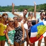 A group of Spanish students stands on the beach of Punta Rucia during one of IIC Spanish School's social activities, waving the Dominican flag, having fun, and enjoying their time together, experiencing the Dominican Republic's beautiful beaches and the great hospitality of its people while learning Spanish in the Dominican Republic.