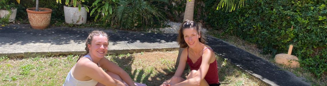 Two girls sitting underneath a palm tree at IIC Spanish School in Santo Domingo who are two of many Spanish students who learn Spanish at IIC in the Dominican Republic and will plant a tree with their course in 2022.
