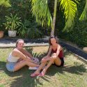 Two girls sitting underneath a palm tree at IIC Spanish School in Santo Domingo who are two of many Spanish students who learn Spanish at IIC in the Dominican Republic and will plant a tree with their course in 2022.